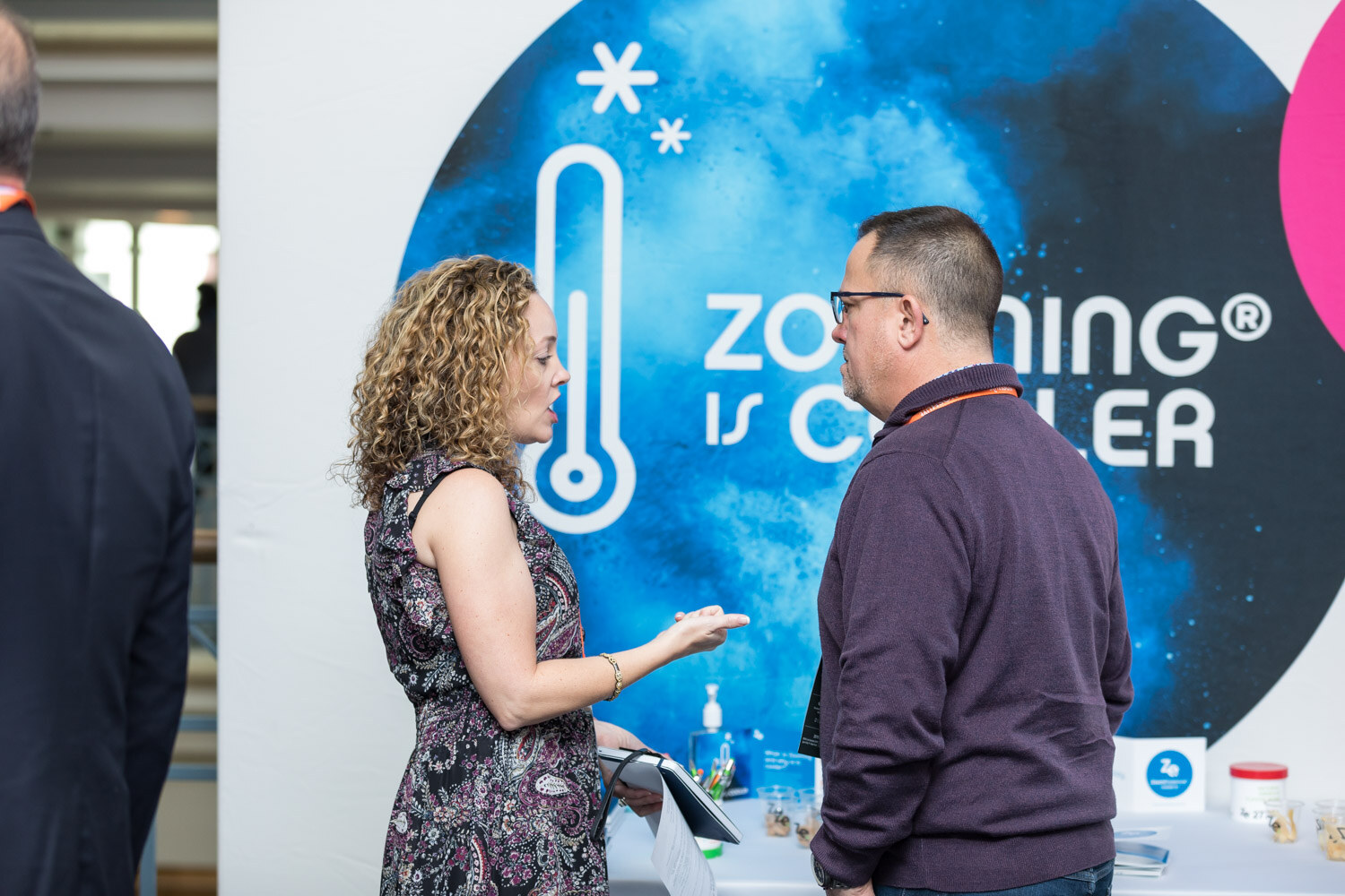 Attendees talk in front of a Zoomessence backdrop reading Zooming is cooler.