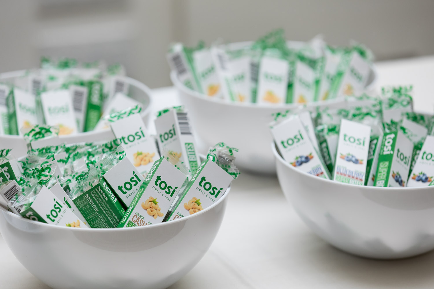 White bowls of Tosi snack packets on an exhibitor table.