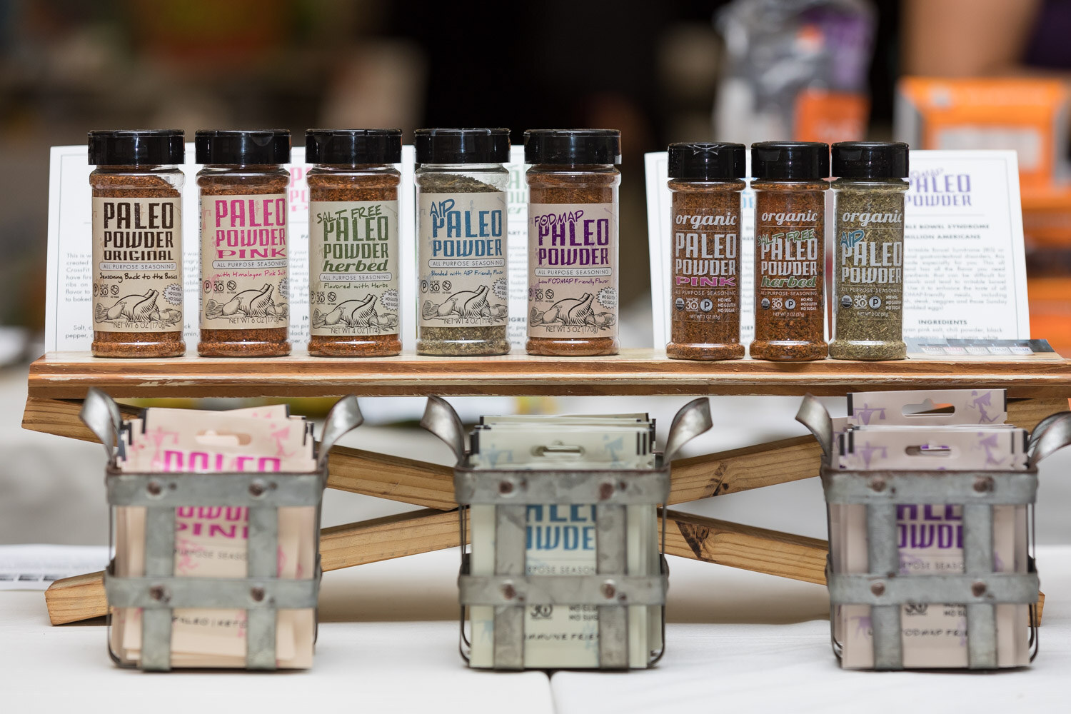 Jars of Paleo Powder seasoning displayed on a wooden stand.