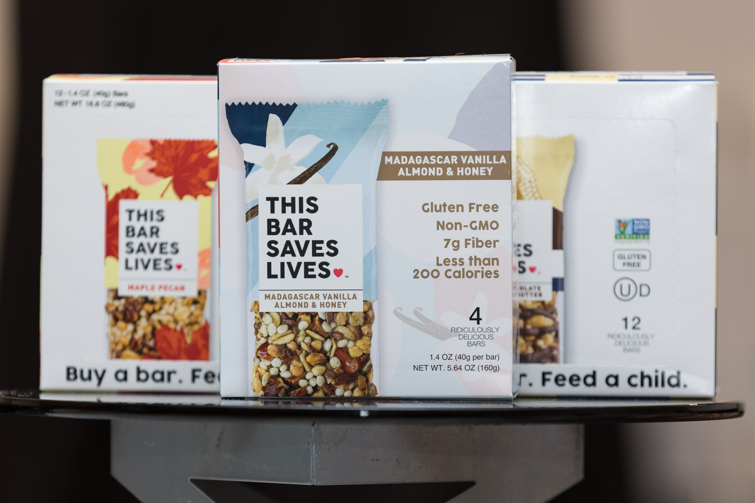 Boxes of This Bar Saves Lives snack bars on a black stand.