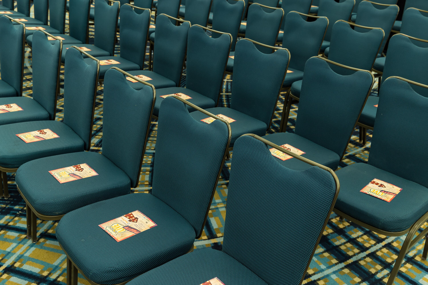 Teal ballroom chairs with a printed card on each seat.