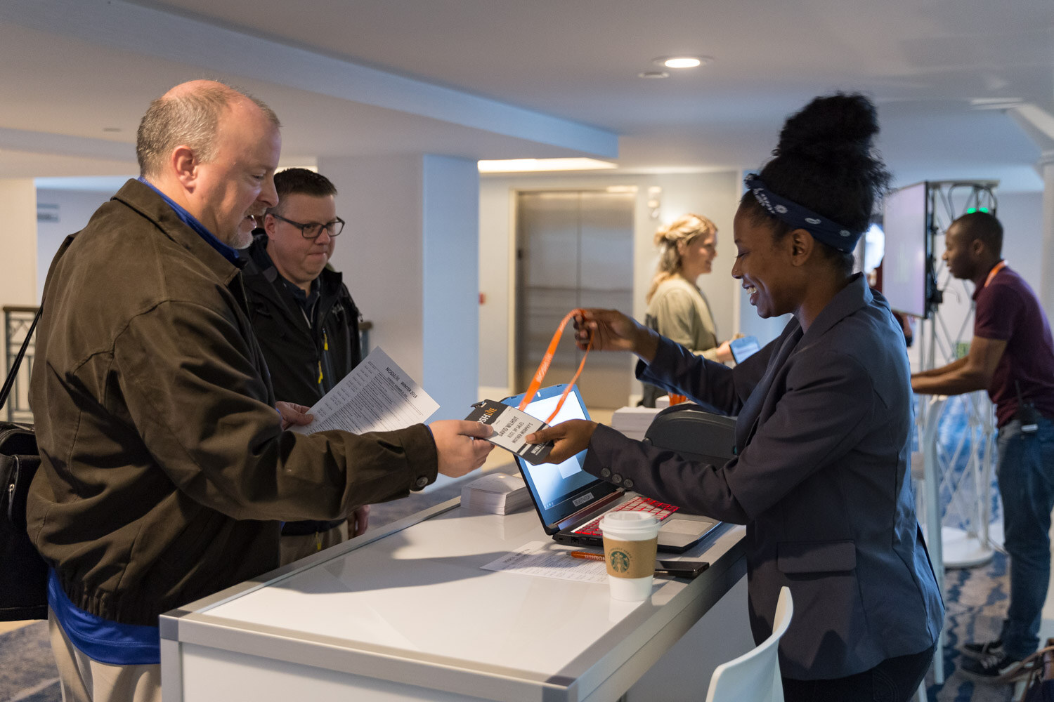 A registration staffer hands a lanyard and badge to an arriving attendee.