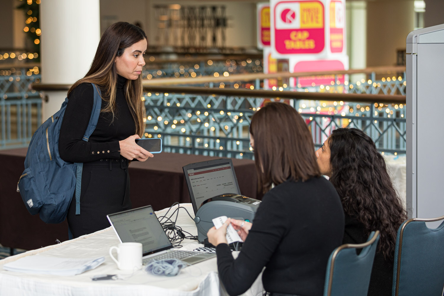 A woman with a backpack checks in at a registration table while two women work at laptops