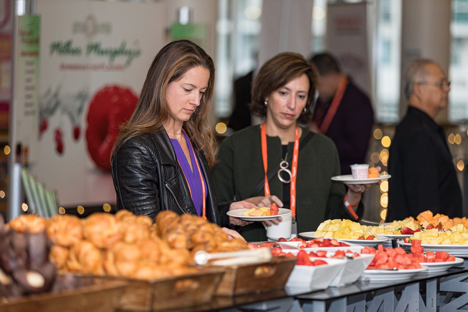 Two women take pastries and fruit from a breakfast buffet in front of a Mother Murphy's banner