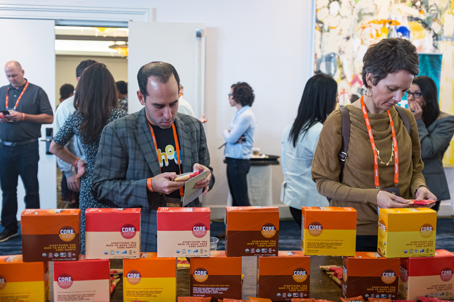 Two attendees browse stacked orange and yellow CORE boxes at a sponsor table