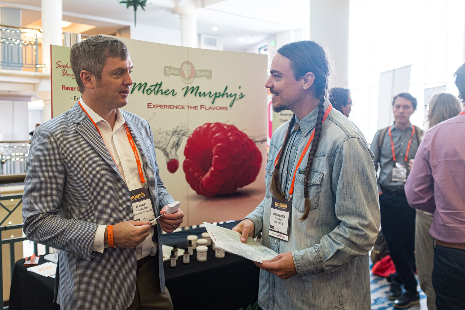 Two men with lanyards talking in front of a Mother Murphy's banner showing a raspberry
