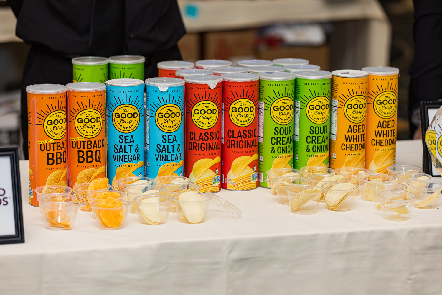 Tall cans of Good Crisp in several flavors lined up with small sample cups in front