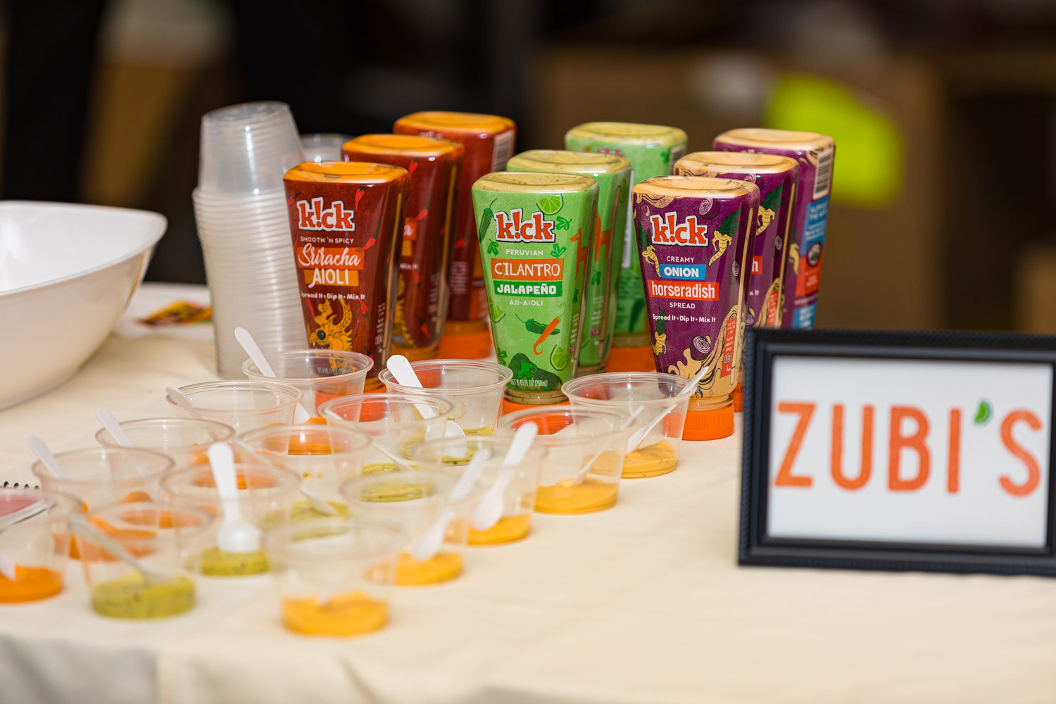 Squeeze bottles of Kick sauces next to cups and a Zubi's sign
