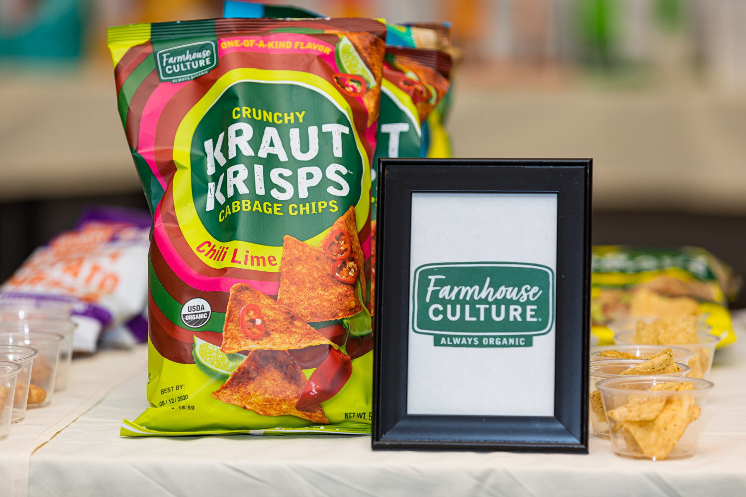 A bag of Farmhouse Culture Kraut Krisps cabbage chips beside a framed Farmhouse Culture sign