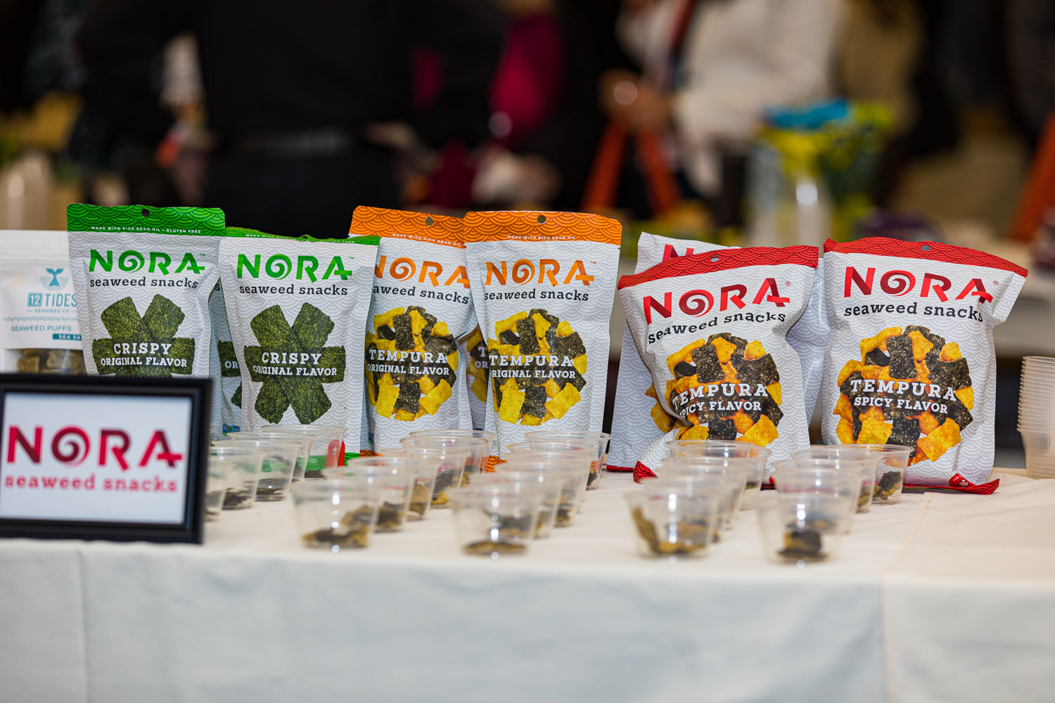 Bags of Nora crispy and tempura seaweed snacks with small sample cups in front