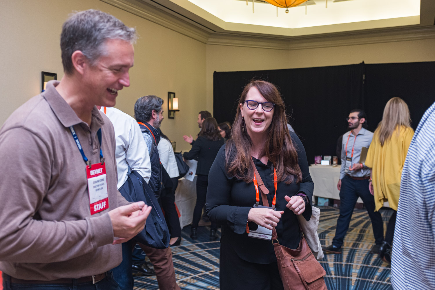 Attendees laughing and chatting between sampling tables in the ballroom