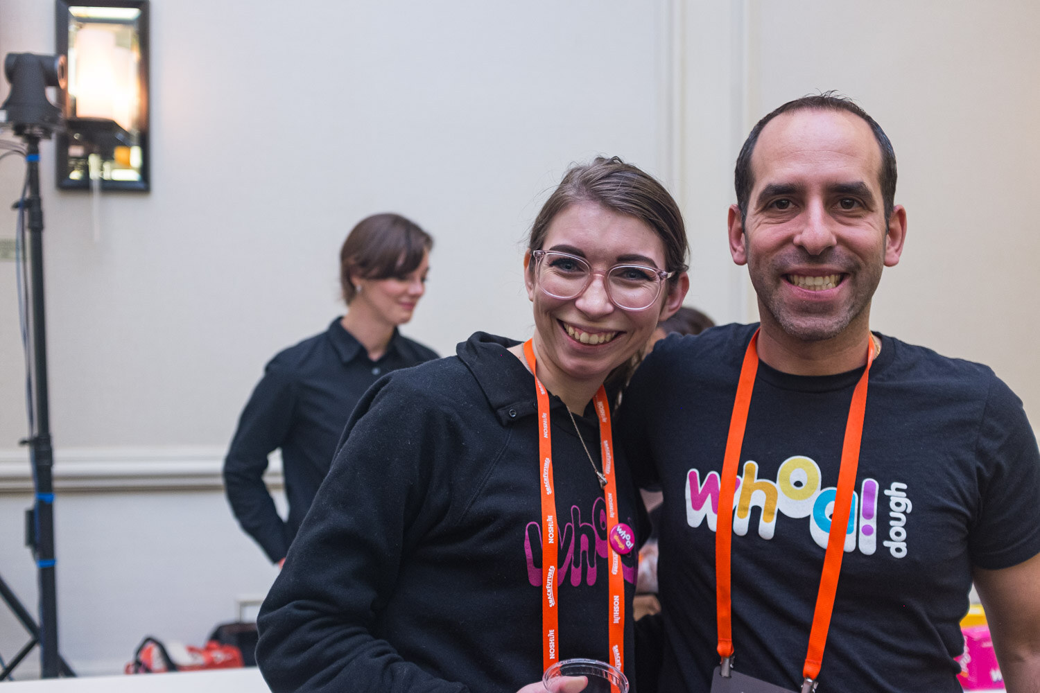 A smiling woman and man in black Whoa Dough shirts with orange lanyards