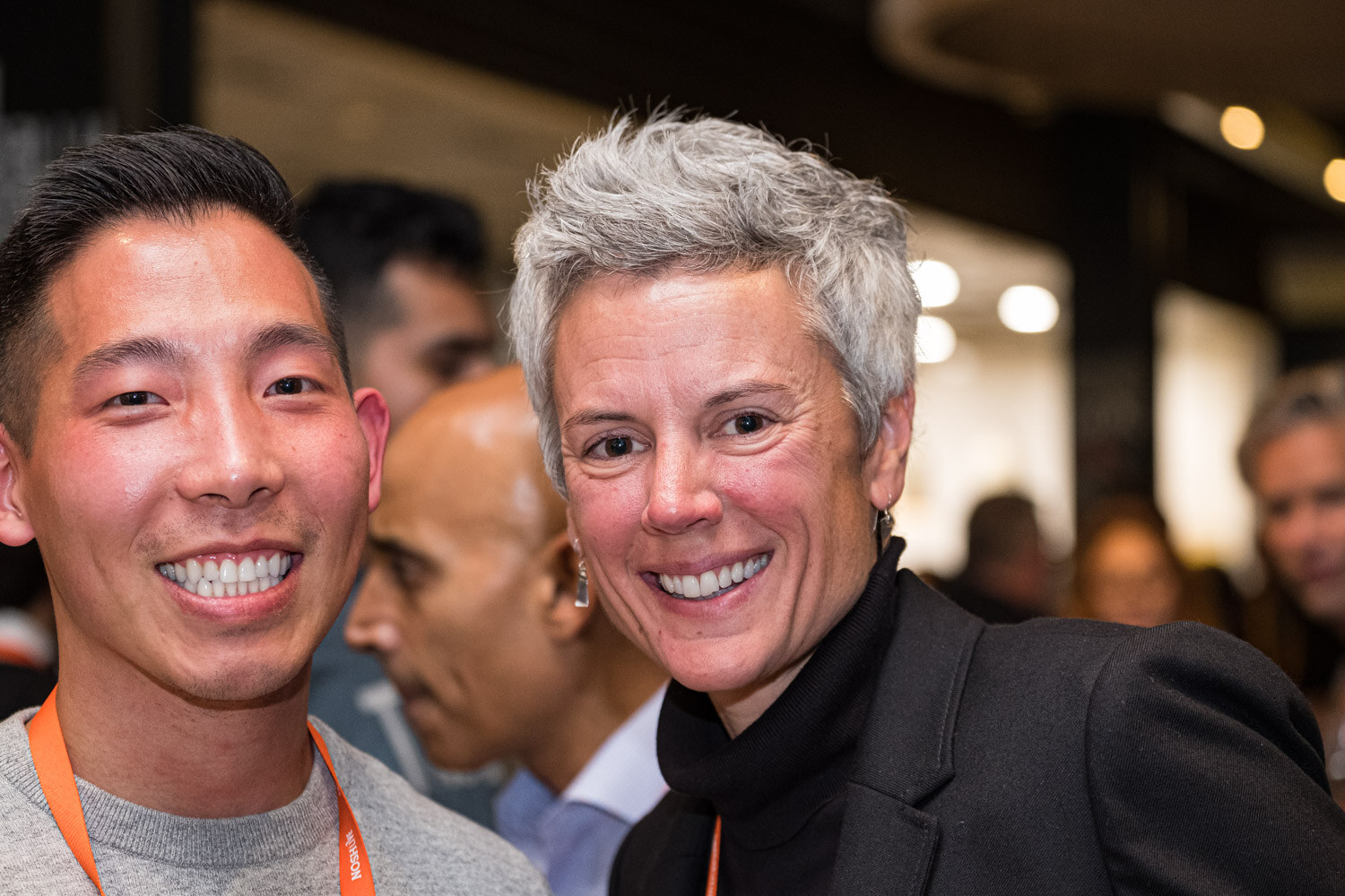 Two smiling people with orange lanyards close together in a dim restaurant