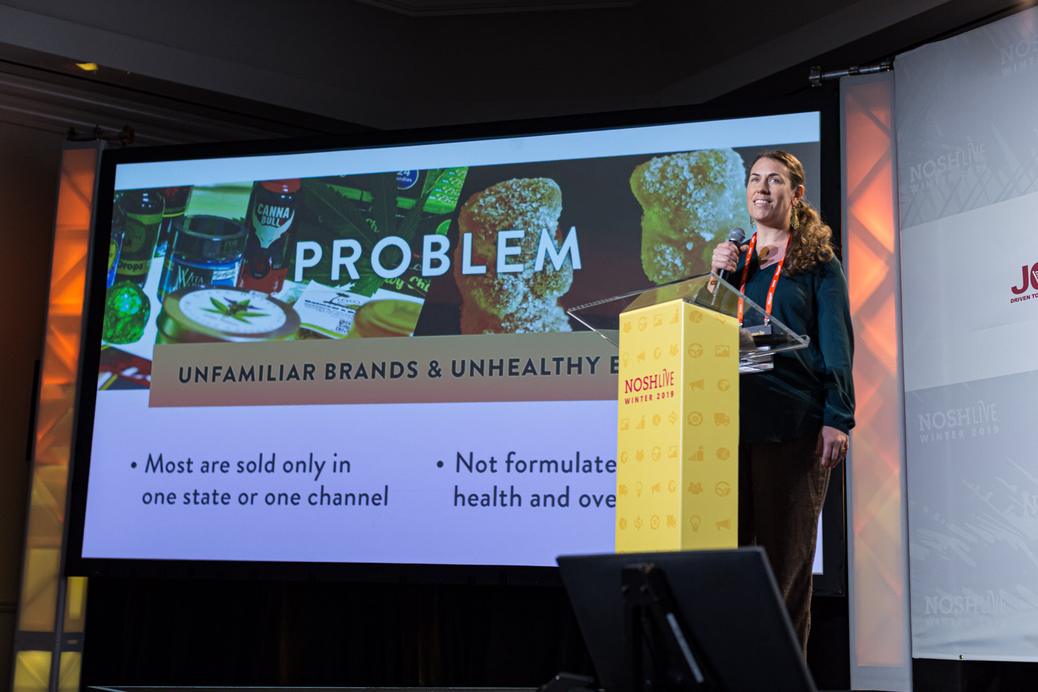 A woman at the Nosh Live lectern next to a slide headed Problem about unfamiliar brands and unhealthy products