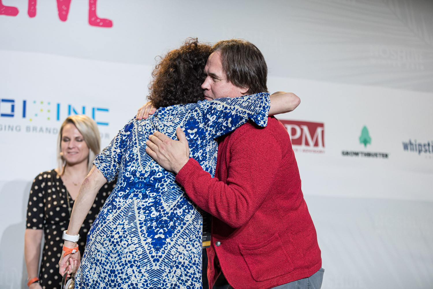 A woman in blue hugs a man in a red cardigan while another judge stands behind