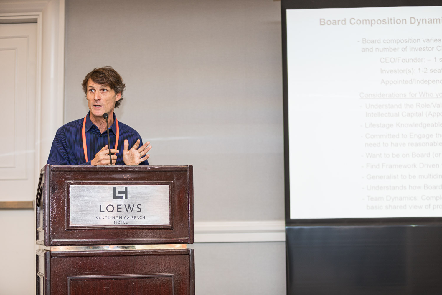 A man at a Loews lectern next to a slide titled Board Composition Dynamics