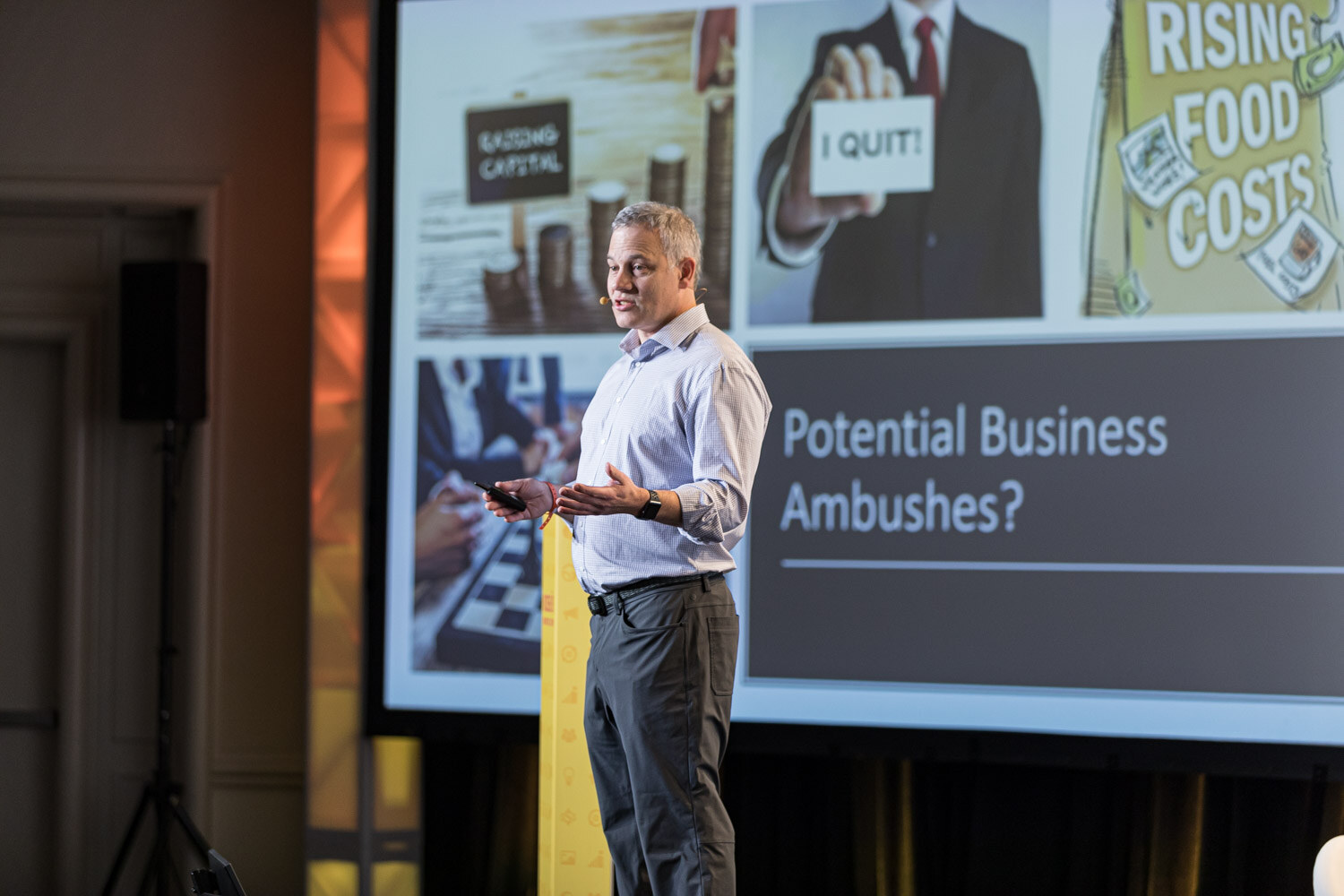 A man standing at the side of the stage in front of a large slide titled Potential Business Ambushes