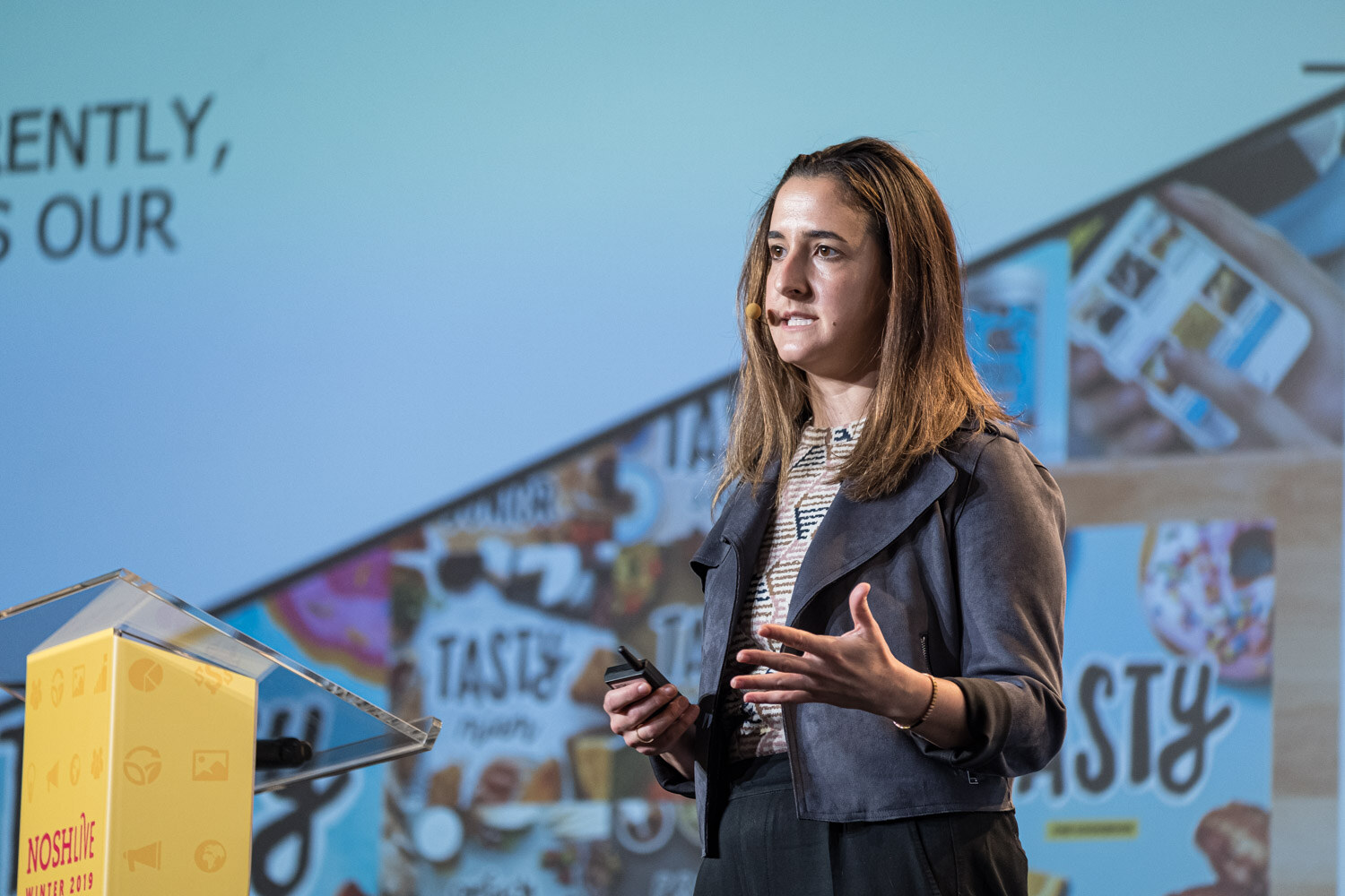 A woman gesturing at the side of the stage with a collage of colorful snack photos behind her
