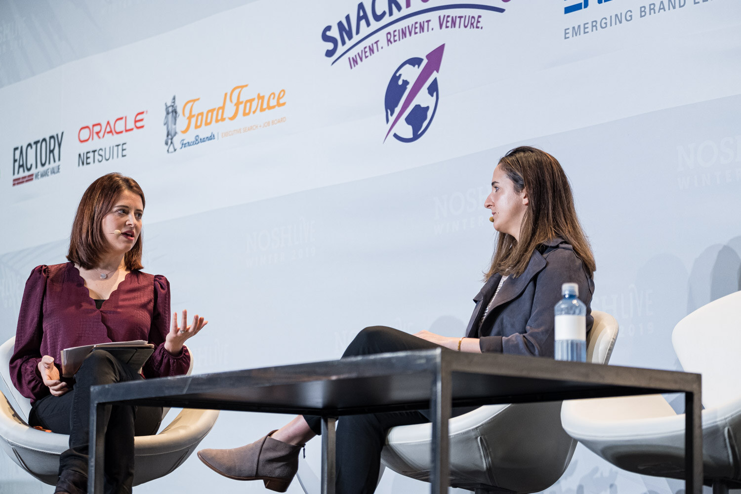 A moderator and a speaker seated across a low table on stage