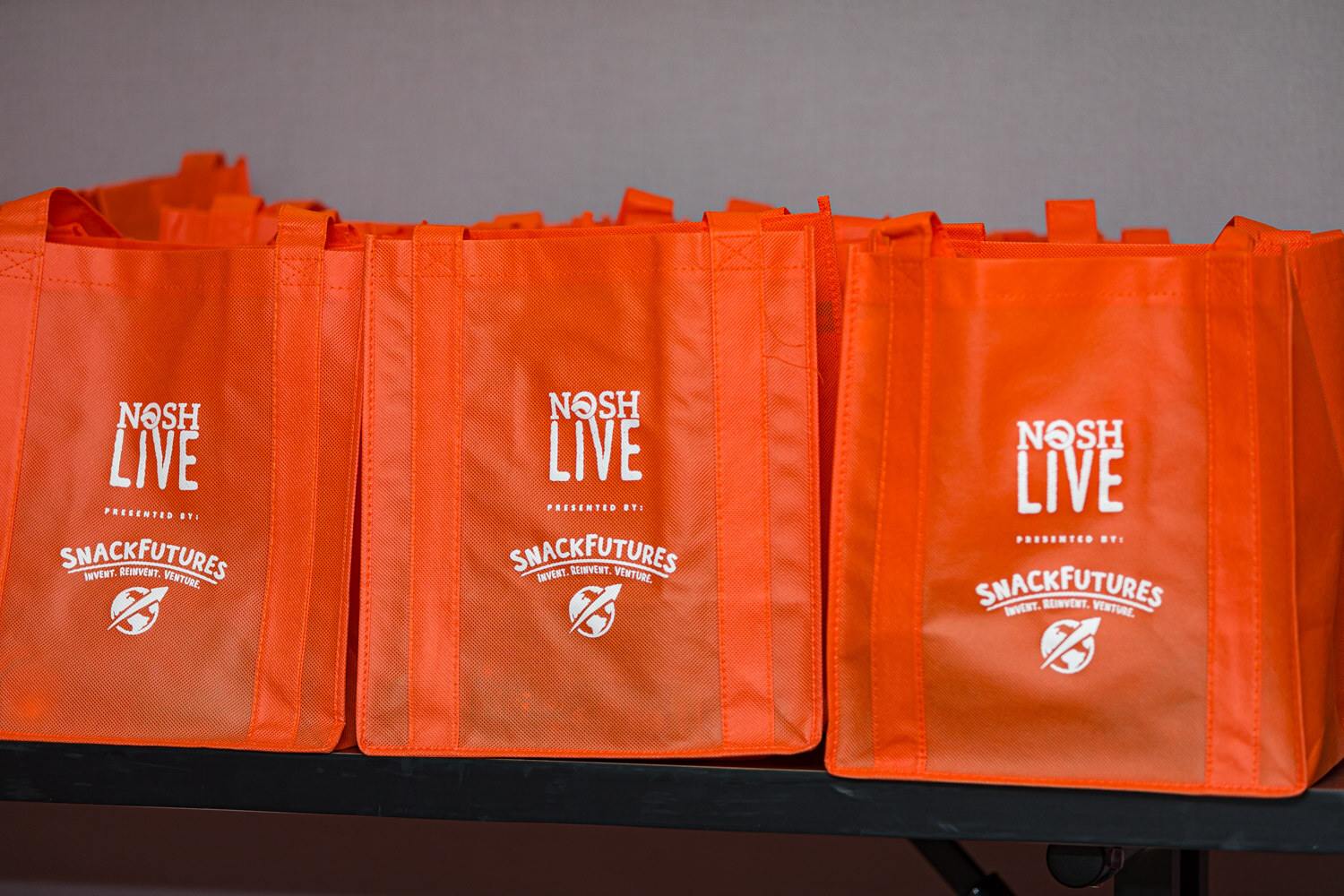 Orange Nosh Live tote bags presented by SnackFutures lined up on a table