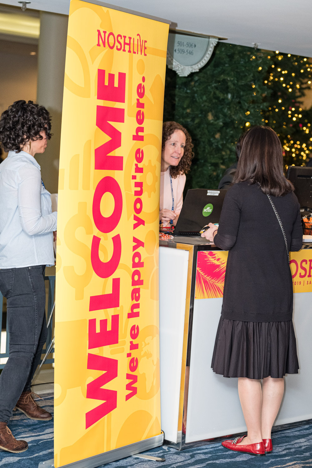 A woman checks in at the registration counter beside a yellow Welcome banner