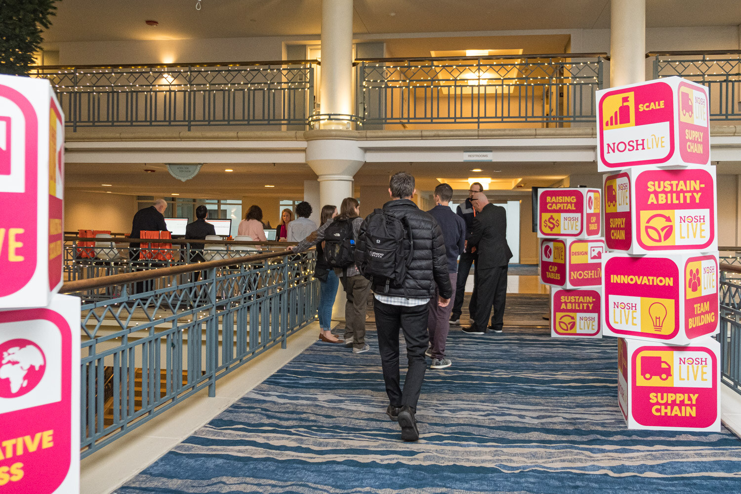 Pink and yellow Nosh Live cubes labeled Sustainability, Innovation and Supply Chain along a balcony walkway