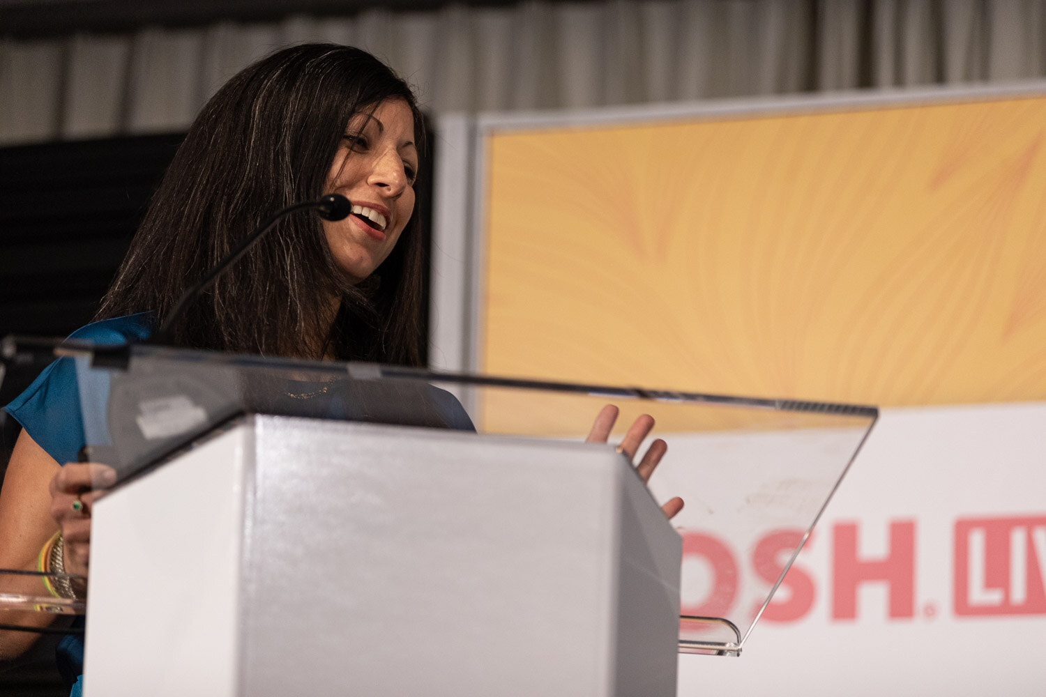 Woman with dark hair behind a clear lectern with a Nosh Live banner behind it.