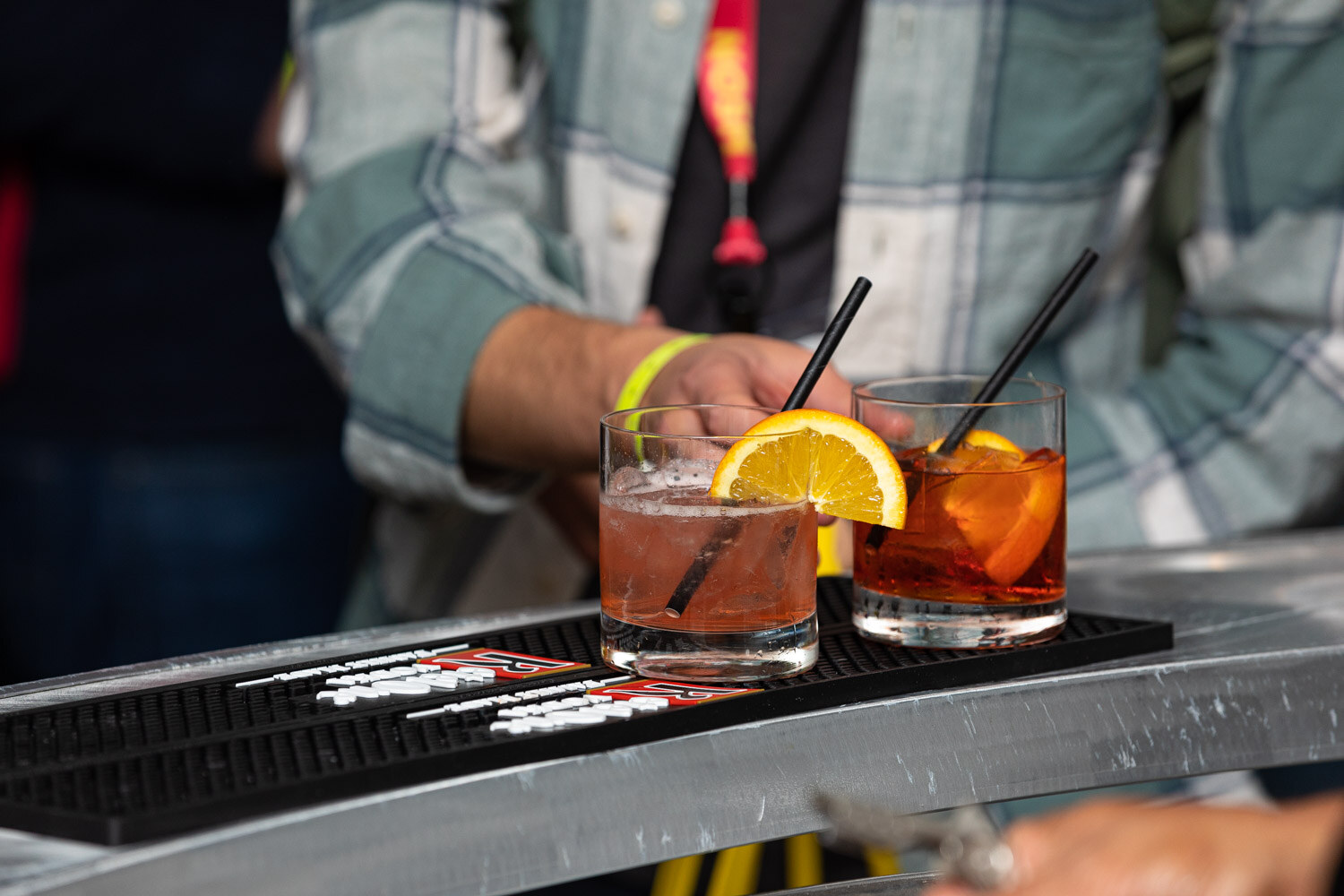 Close-up of two cocktail glasses with orange slices and black straws on a bar mat.