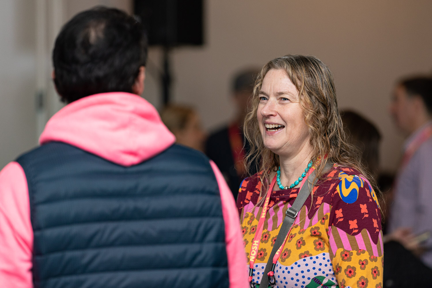 Woman in a colorful patterned top laughing, facing a man in a navy vest over a pink hoodie.