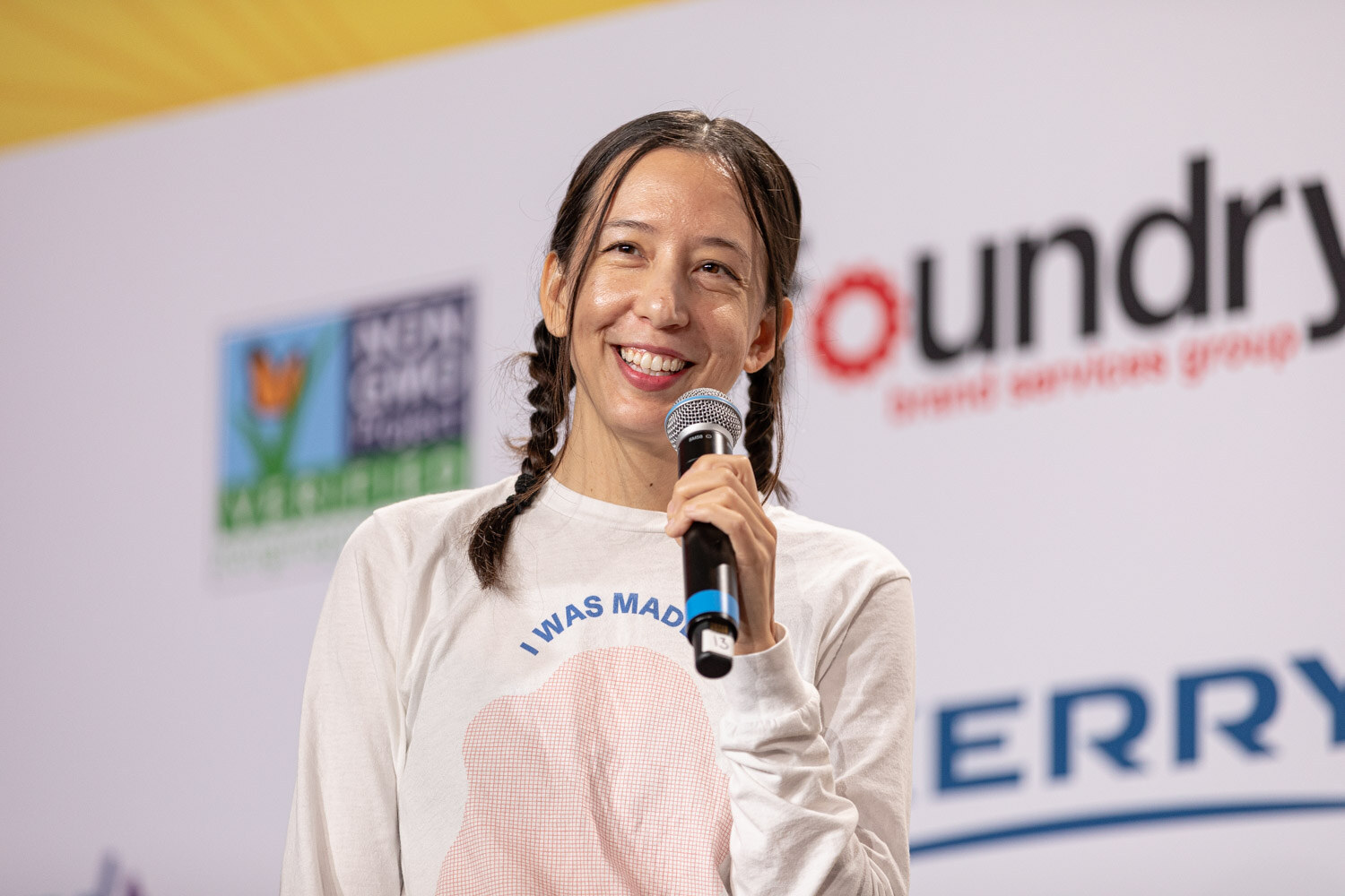 Smiling woman with braids and a white sweatshirt holding a microphone.