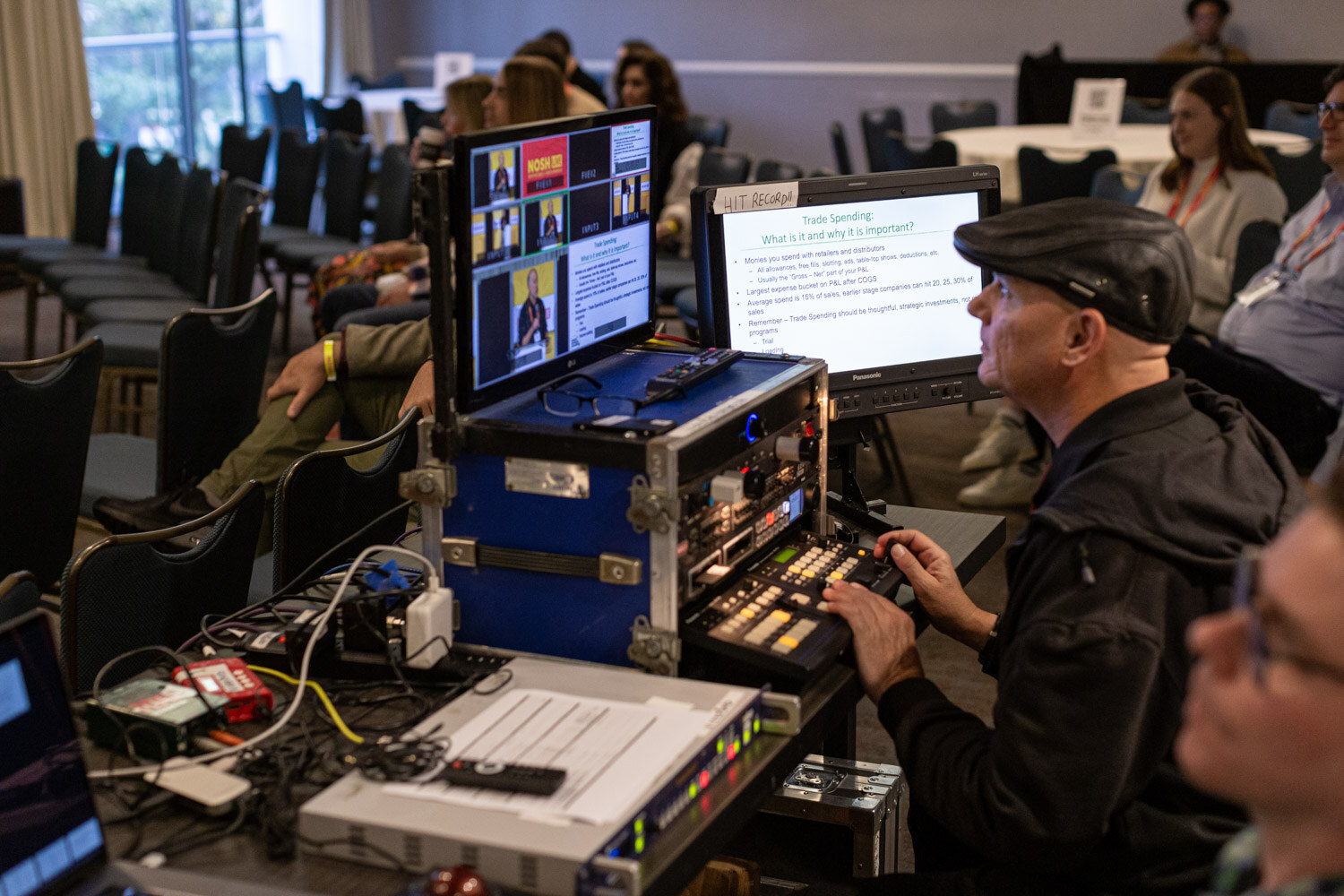 Man in a flat cap operating a video switching console with monitors showing the stage feed.