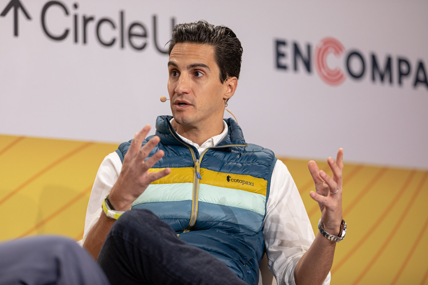 Man in a blue and yellow striped vest gesturing with both hands, in front of Circle Up and Encompass logos.