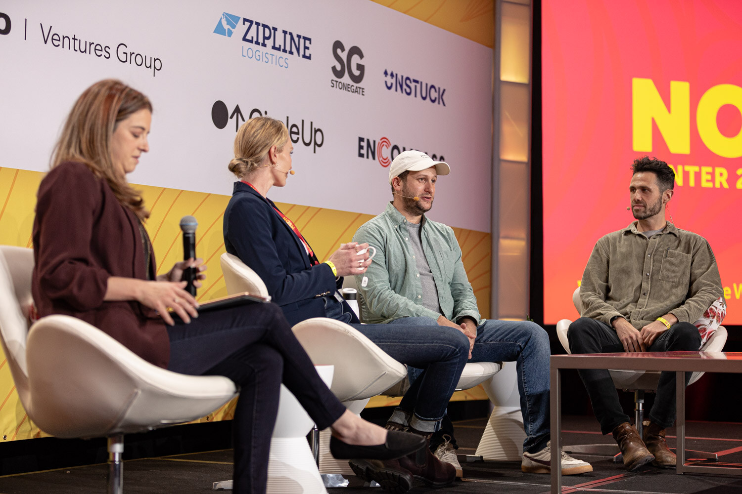 Four people seated on stage with sponsor logos behind them and a Nosh Live screen at the edge.
