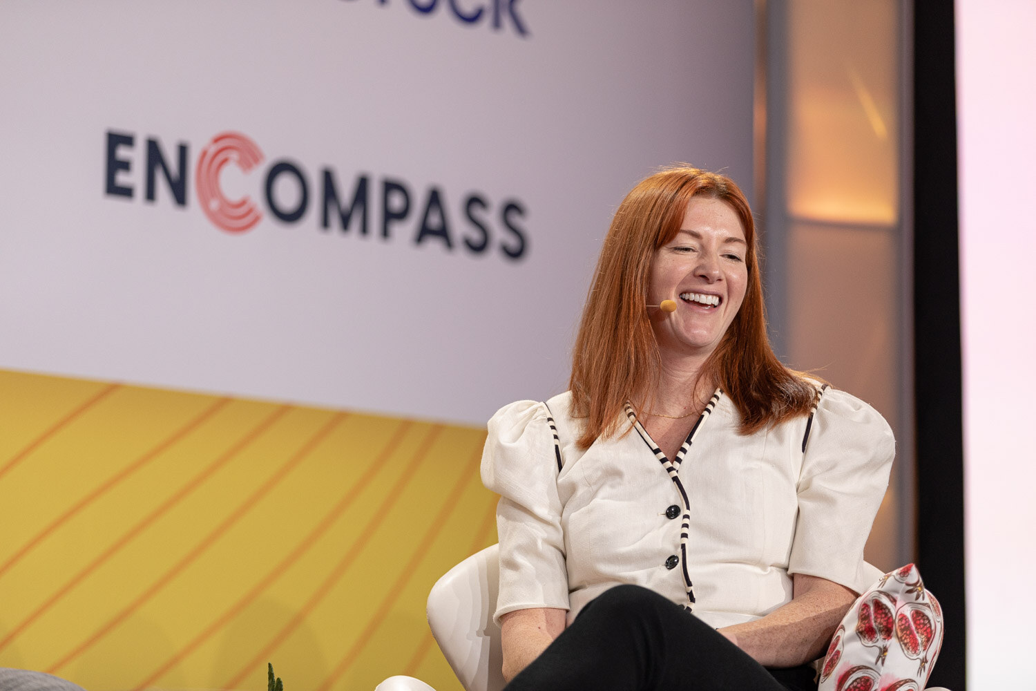 Red-haired woman in a white blouse laughing while seated in front of an Encompass logo.