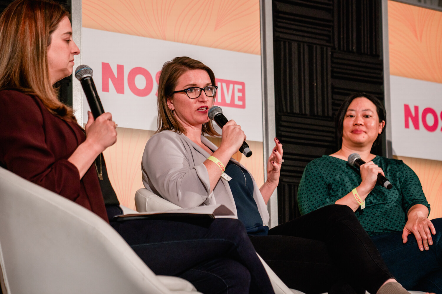 Three women holding microphones seated close together, one gesturing as she speaks.