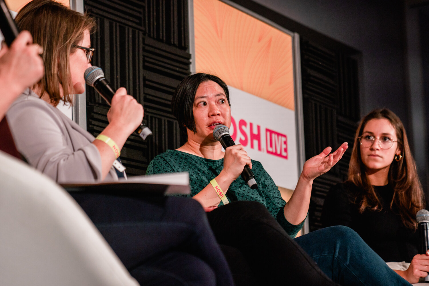 Woman in a green top speaking into a microphone with another panelist listening beside her.