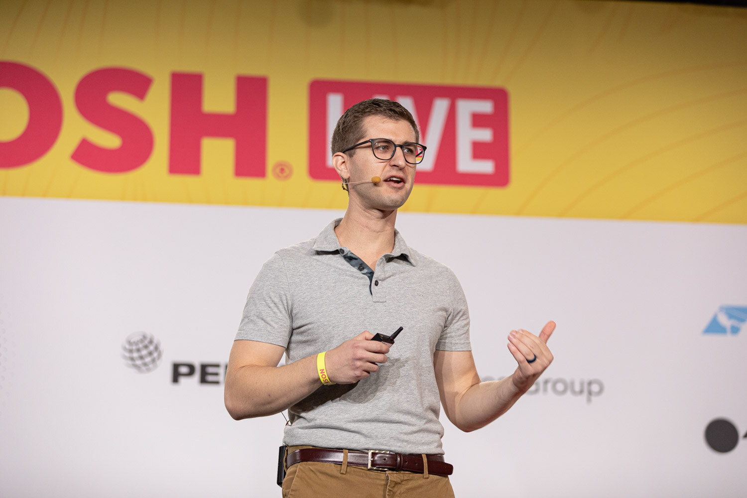 Man in glasses and a gray polo holding a clicker in front of a Nosh Live banner.