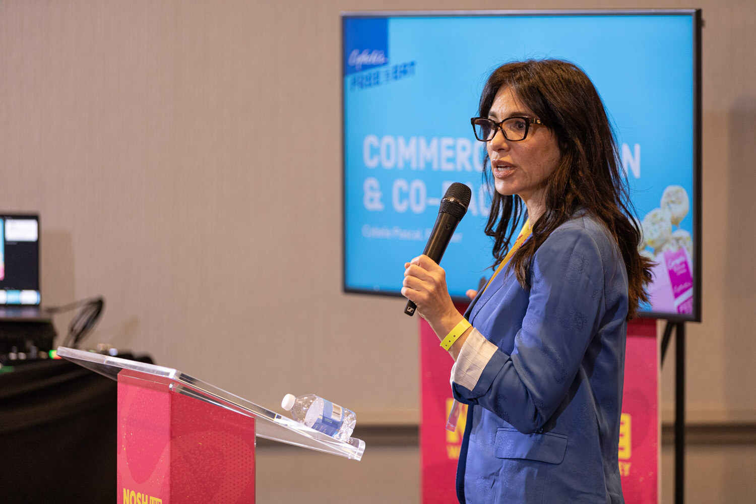 A woman presenting beside a screen with a slide titled Commercialization and Co-Packing.