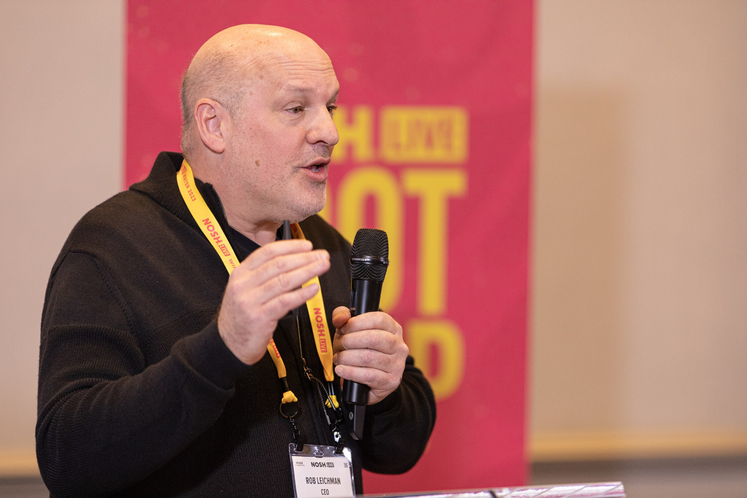 A man in a black sweater speaking into a microphone in front of a Boot Camp banner.