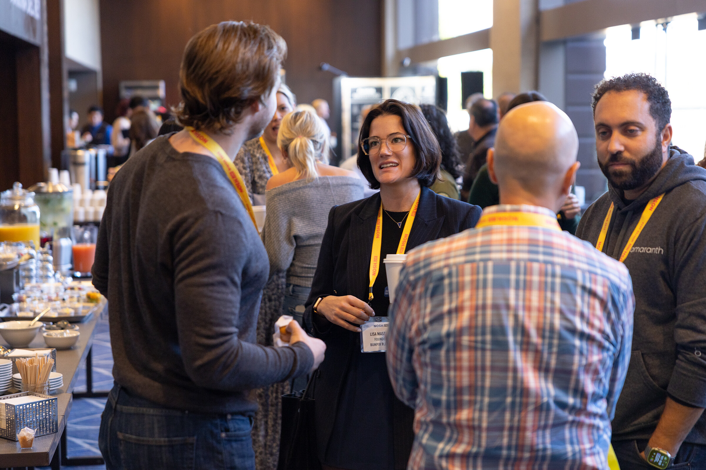 Four attendees with lanyards talking beside a breakfast buffet table.