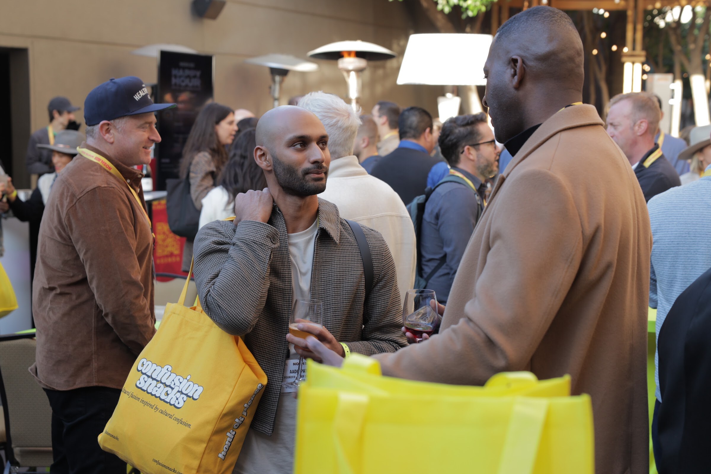 A group of attendees talking at a crowded outdoor reception, one holding a drink.