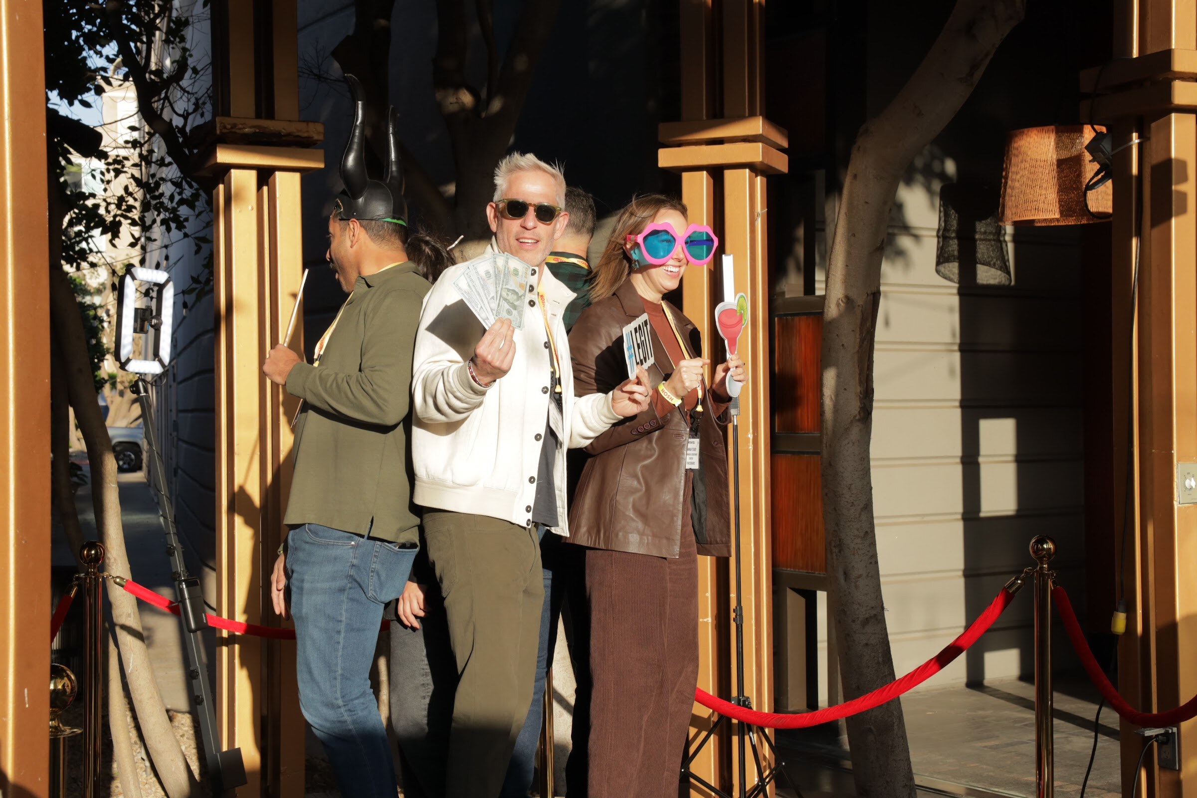 Three people posing with cash and novelty sunglasses in front of a red velvet rope.