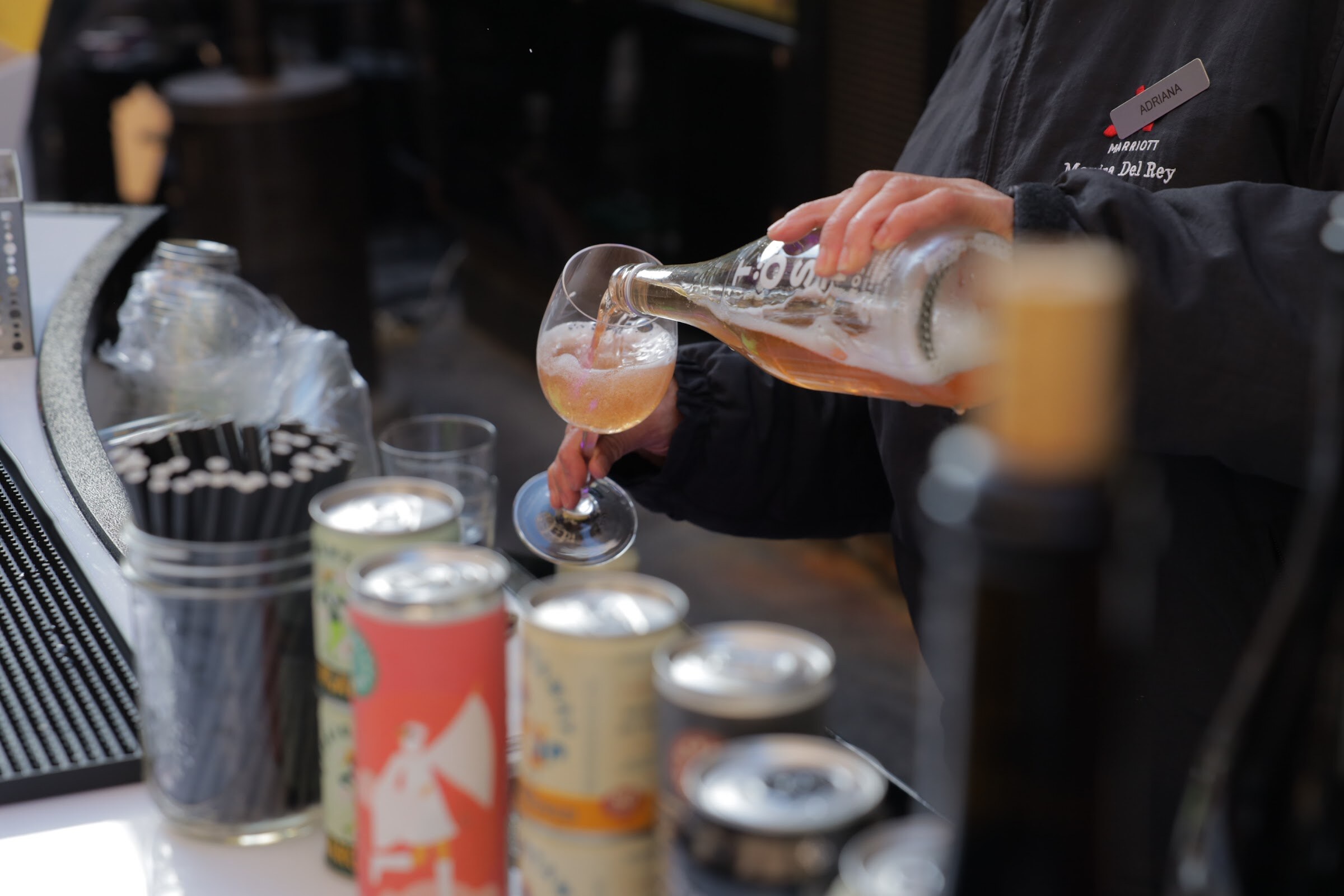 A hand pouring a drink into a stemmed glass next to several beverage cans.