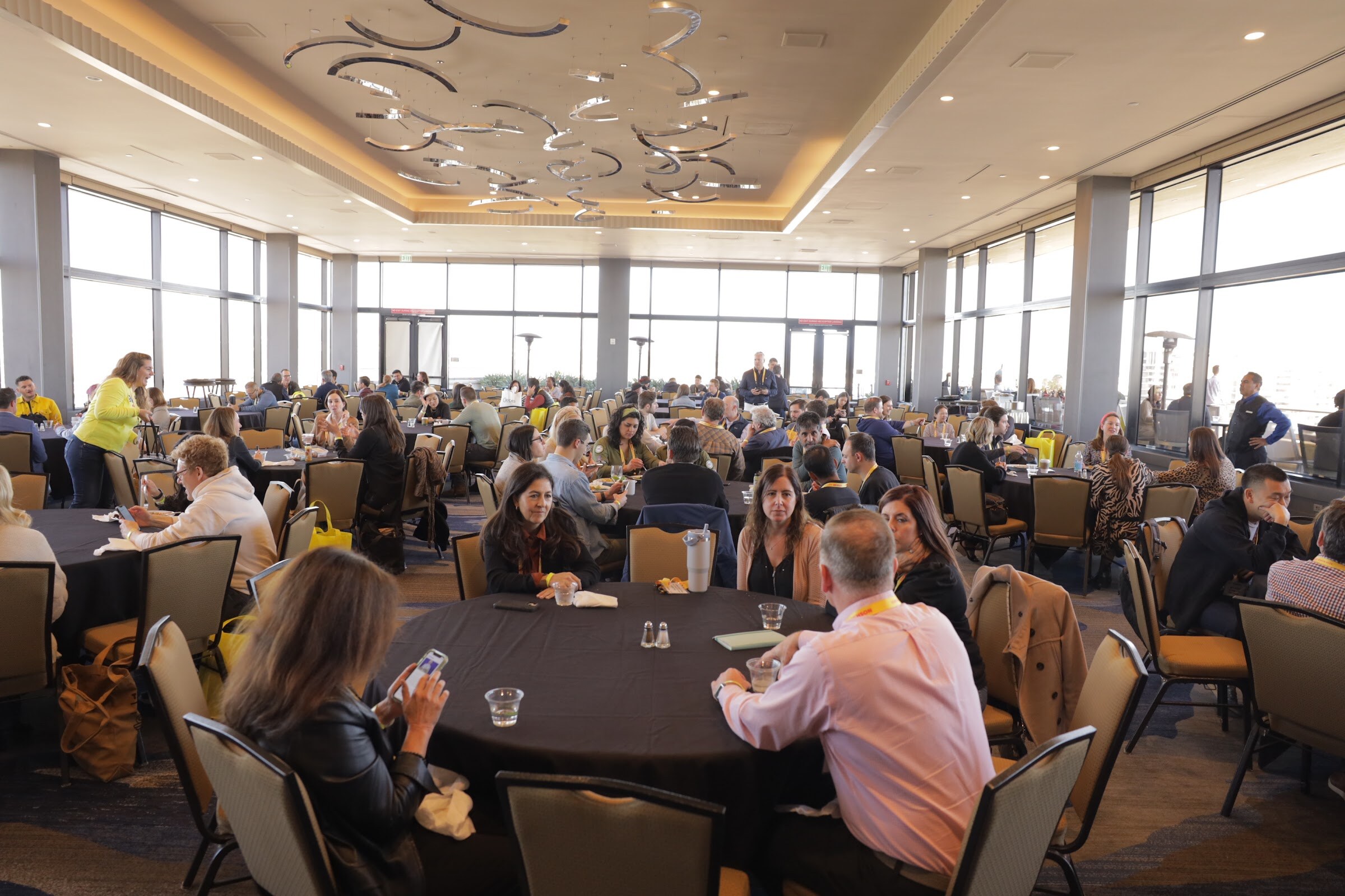 A large ballroom with round tables where attendees are seated for lunch.