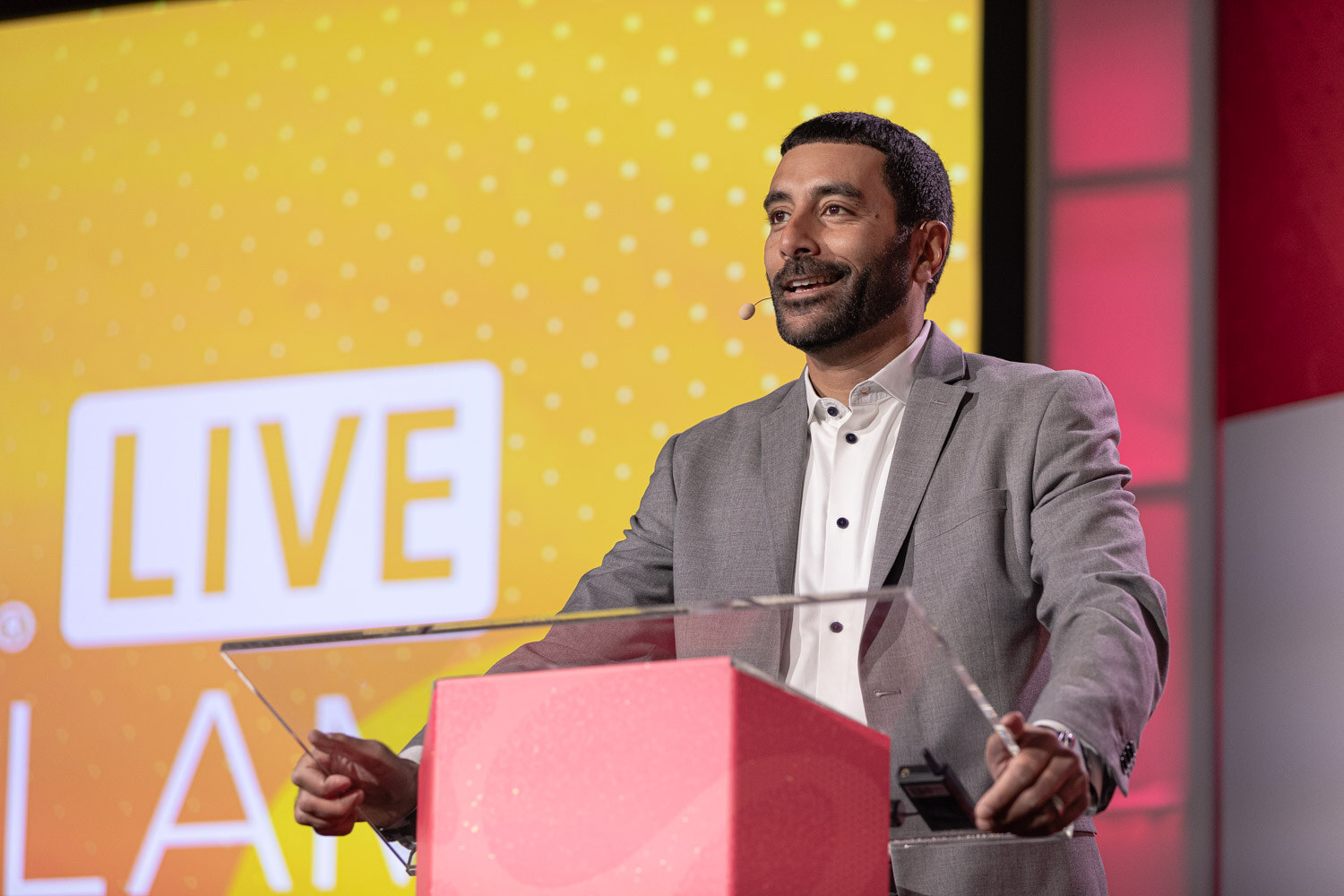 A man in a gray blazer speaking at a podium in front of a NOSH LIVE Pitch Slam screen.
