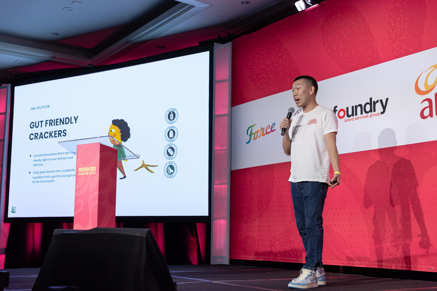 A man standing on stage beside a slide titled Gut Friendly Crackers.