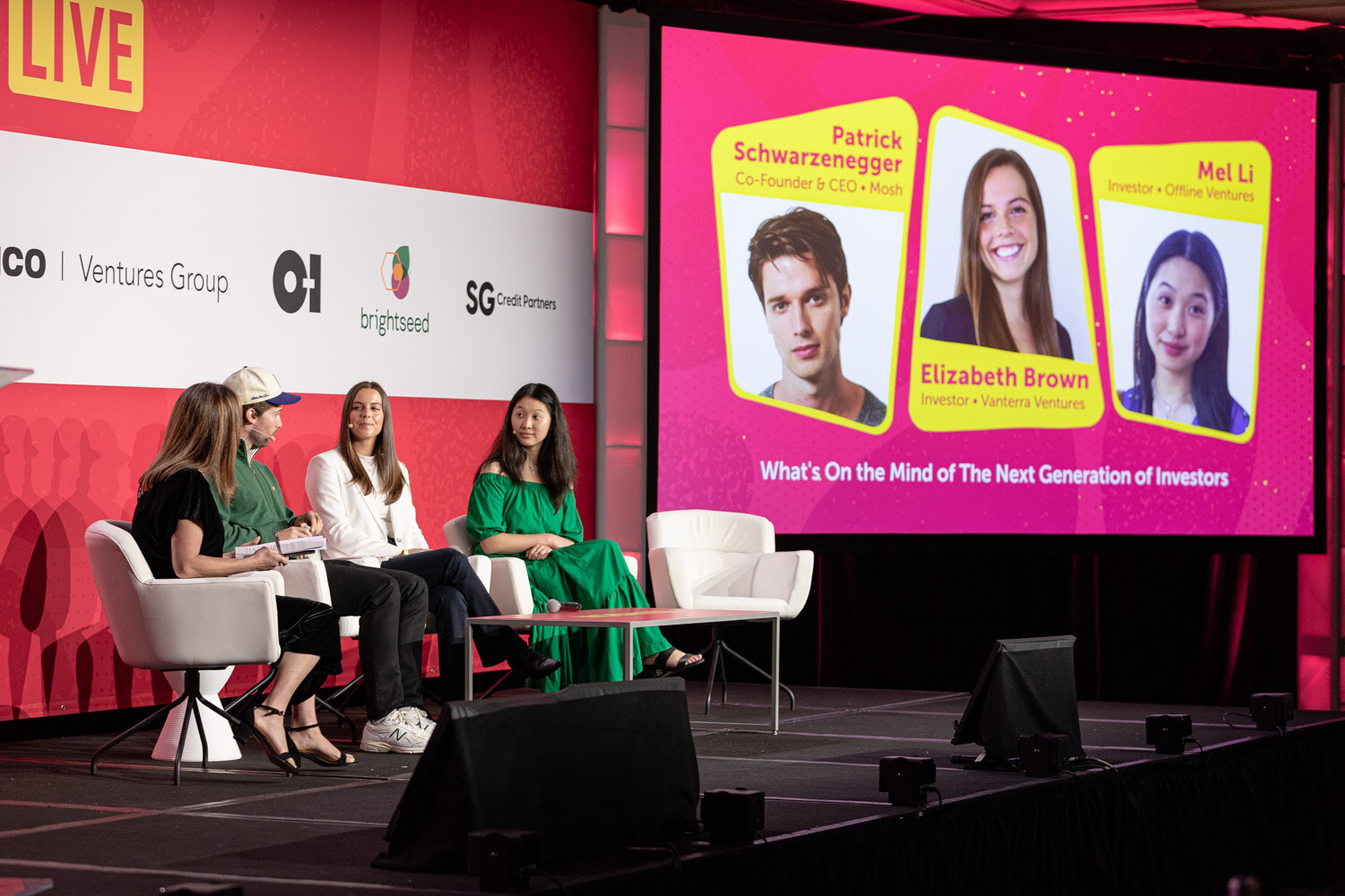 Four people seated on stage with a screen introducing the panelists.