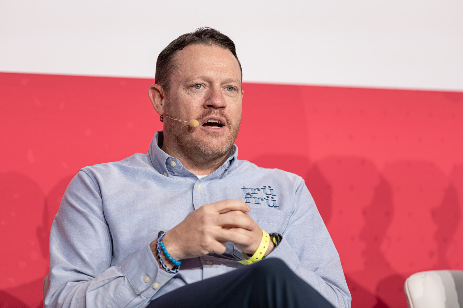 A man in a light blue shirt gesturing while speaking on stage.