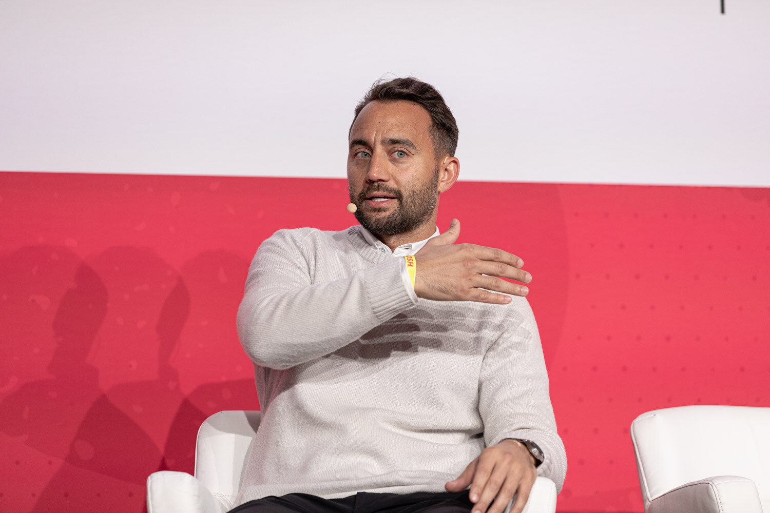 A man in a white sweater gesturing with both hands while seated.