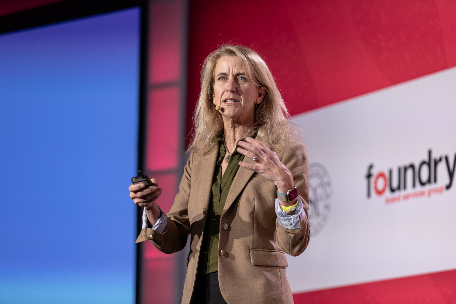 A woman in a tan blazer gesturing with a clicker in her hand.